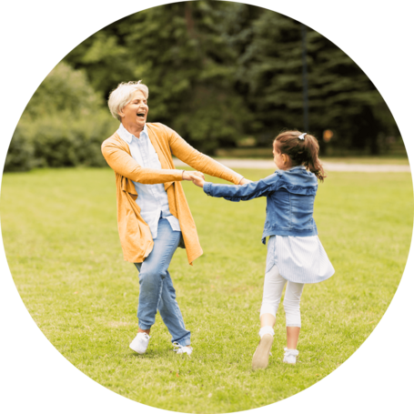 Happy grandmother and granddaughter holding hands and spinning around in a grassy park, enjoying a playful moment together.